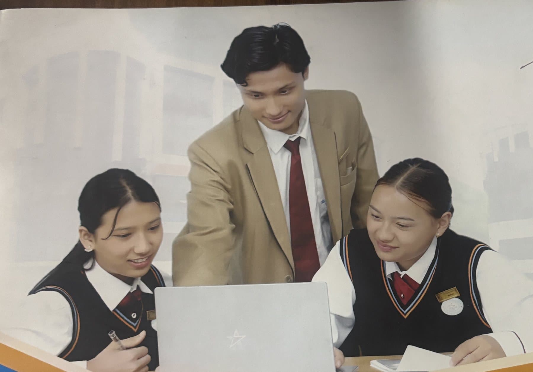 Two students and a teacher gathered around a laptop in SWSC uniform